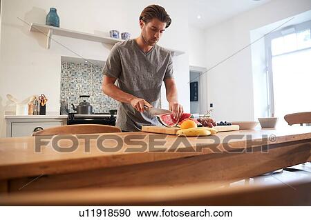 Young man slicing fresh watermelon at kitchen table View Large Photo Image Stock Image - Young man slicing fresh watermelon at kitchen table. Fotosearch