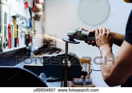 Stock Photo - Young man using angle grinder on metal in workshop, cropped. Fotosearch