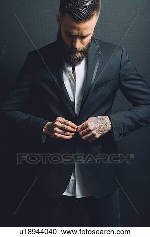 Stock Image - Young man wearing suit, doing up suit jacket, tattoos on hands. Fotosearch