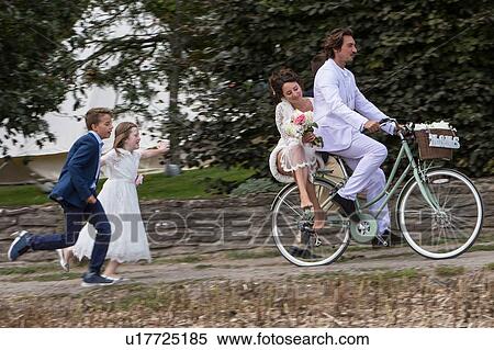 Stock Photography - Young wedding guests running after newlyweds on bicycles. Fotosearch