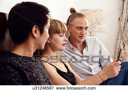 Young woman and male friends looking at smartphone on bed View Large Photo Image Stock Photo - Young woman and male friends looking at smartphone on bed. Fotosearch