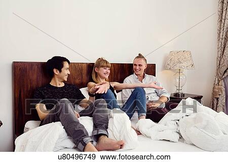 Young woman and male friends sitting chatting on bed View Large Photo Image Stock Photo - Young woman and male friends sitting chatting on bed. Fotosearch