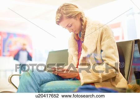 Young woman at airport, sitting, using smartphone View Large Photo Image Stock Image - Young woman at airport, sitting, using smartphone. Fotosearch