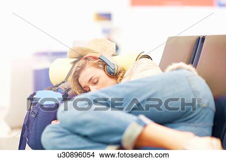 Picture - Young woman at airport, sleeping on seating in departure lounge. Fotosearch