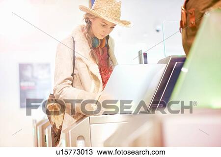 Stock Image - Young woman at airport, walking through turnstile. Fotosearch