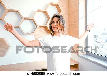 Stock Image - Young woman at home, arms outstretched, smiling. Fotosearch