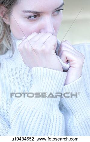 Stock Image - Young woman clasping neck of sweater. Fotosearch
