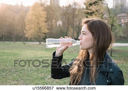 Young woman drinking from water bottle in park View Large Photo Image Stock Photo - Young woman drinking from water bottle in park. Fotosearch