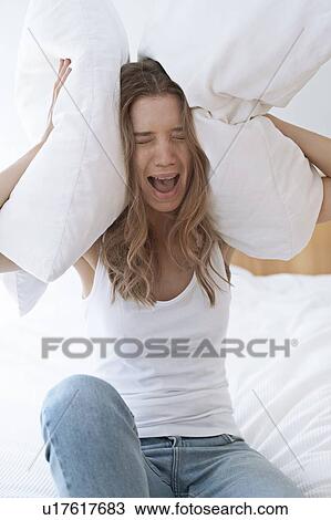 Stock Image - Young woman holding pillow over her ears and screaming. Fotosearch