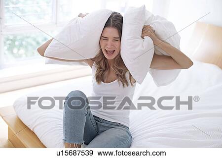 Young woman holding pillow over her ears and screaming View Large Photo Image Stock Photo - Young woman holding pillow over her ears and screaming. Fotosearch