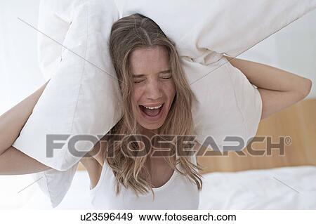 Young woman holding pillow over her ears and screaming View Large Photo Image Stock Photo - Young woman holding pillow over her ears and screaming. Fotosearch