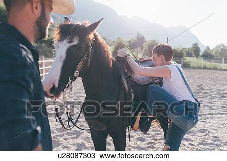 Young woman mounting horse in rural equestrian arena View Large Photo Image Stock Image - Young woman mounting horse in rural equestrian arena. Fotosearch