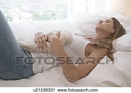 Stock Photo - Young woman on bed with hot water bottle on tummy. Fotosearch
