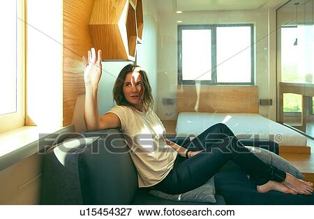 Stock Photo - Young woman relaxing at home, holding hand up to stop sunlight shining on face. Fotosearch