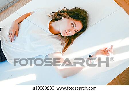 Stock Photograph - Young woman relaxing on bed, arm resting in ray of light, thoughtful ex0ession. Fotosearch
