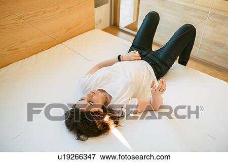 Stock Photo - Young woman relaxing on bed, thoughtful ex0ession. Fotosearch
