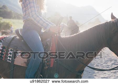 Stock Photo - Young woman riding horse in sunlit equestrian arena, cropped, Primaluna, Trentino-Alto Adige, Italy. Fotosearch