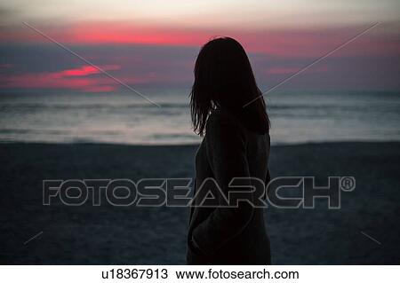 Young woman standing alone on beach, watching sunrise, rear view View Large Photo Image Stock Image - Young woman standing alone on beach, watching sunrise, rear view. Fotosearch