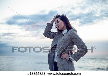 Young woman standing on beach, hand keeping hair from face, thoughtful ex0ession View Large Photo Image Stock Photo - Young woman standing on beach, hand keeping hair from face, thoughtful ex0ession. Fotosearch