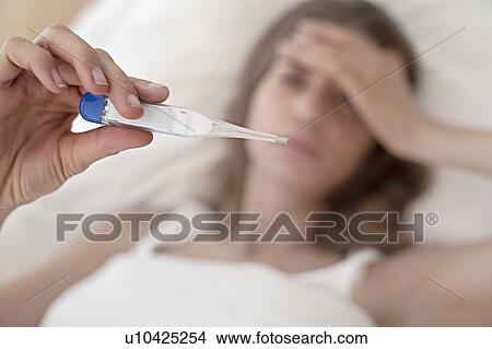 Picture - Young woman taking her temperature. Fotosearch