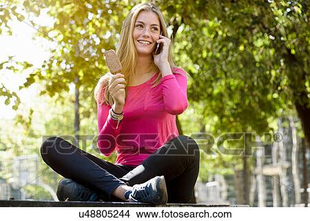 Picture - Young woman talking on smartphone in park. Fotosearch
