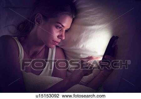 Stock Image - Young woman using digital tablet in bed. Fotosearch