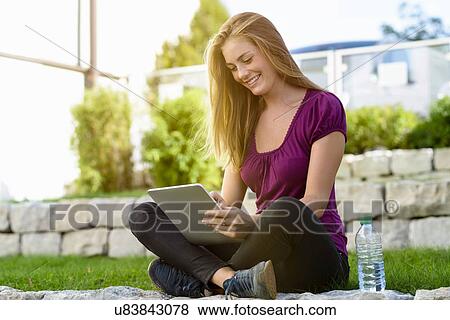 Stock Photo - Young woman using digital tablet in park. Fotosearch