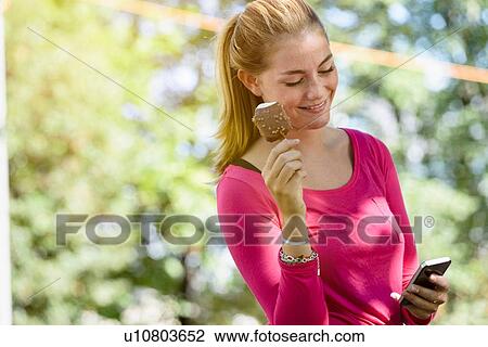 Stock Image - Young woman using smartphone in park. Fotosearch