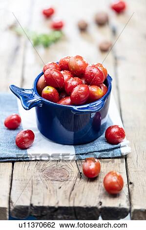 Stock Image - Baby plum tomatoes in blue bowl, still life. Fotosearch
