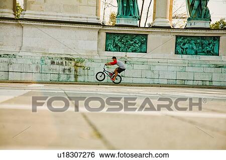 Stock Photograph - BMX cyclist doing wheelie, Heroes Square (Hosk Tere), Budapest, Hungary. Fotosearch