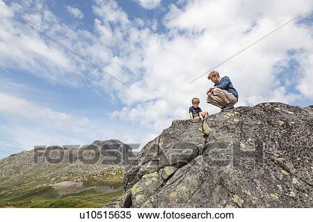 Boy and father crouching on top of rock formation, low angle view, Oppland, Nord-Trondelag, Norway View Large Photo Image Stock Photography - Boy and father crouching on top of rock formation, low angle view, Oppland, Nord-Trondelag, Norway. Fotosearch