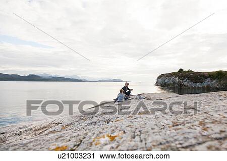 Stock Image - Boy and father eating food on inlet rock, Aure, More og Romsdal, Norway. Fotosearch