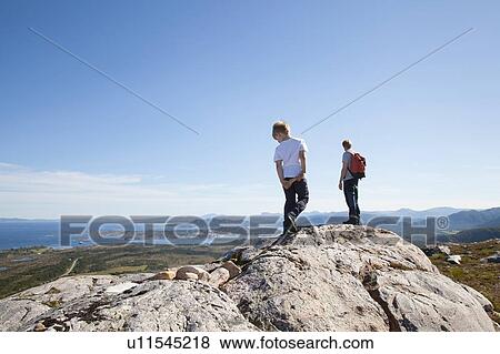 Stock Photo - Boy and father looking out from rock formation over landscape, Aure, More og Romsdal, Norway. Fotosearch