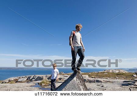 Stock Image - Boy and father looking out from top of rock formation over landscape, Aure, More og Romsdal, Norway. Fotosearch