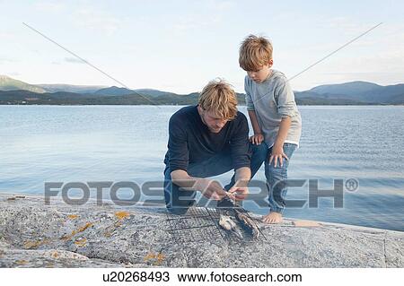 Stock Image - Boy and father preparing fish to grill on inlet rock, Aure, More og Romsdal, Norway. Fotosearch