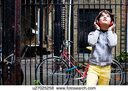 Stock Photo - Boy listening to music with headphones, bicycle in background. Fotosearch