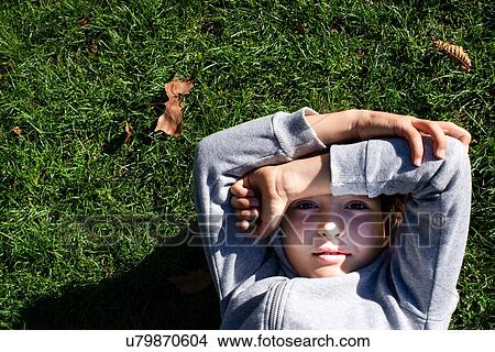 Picture - Boy on grass blocking sunlight with arms. Fotosearch