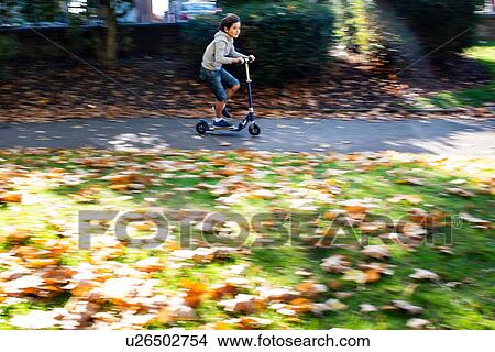 Boy riding push scooter in park View Large Photo Image Picture - Boy riding push scooter in park. Fotosearch