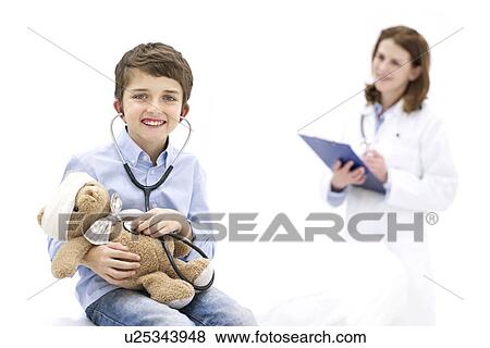 Boy role playing with teddy bear and stethoscope with doctor in background. View Large Photo Image Stock Photo - Boy role playing with teddy bear and stethoscope with doctor in background.. Fotosearch