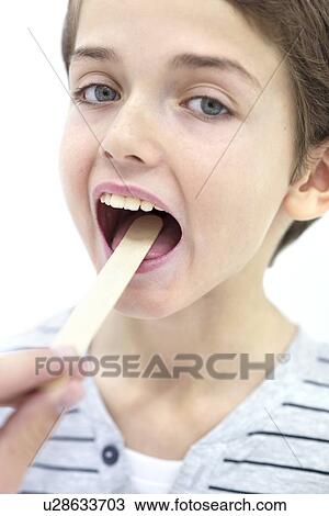 Stock Image - Boy with mouth open and tongue depressor.. Fotosearch