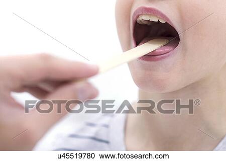 Stock Image - Boy with mouth open and tongue depressor.. Fotosearch
