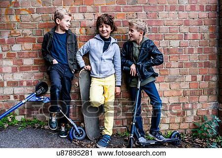 Stock Image - Boys leaning against brickwall. Fotosearch