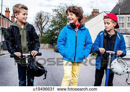 Stock Image - Boys riding push scooter on street. Fotosearch