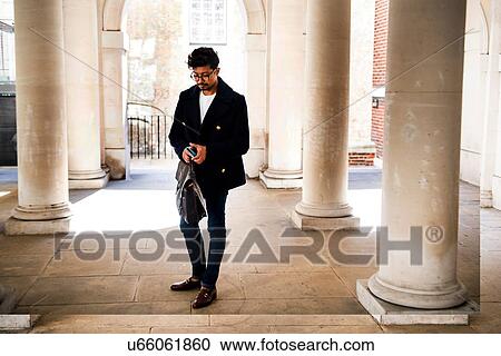 Stock Image - Businessman using smartphone in city. Fotosearch