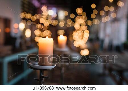 Stock Photo - Close up of lit candle in cafe with decorative lights. Fotosearch