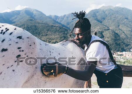 Stock Photograph - Cool young man grooming horse in rural equestrian arena, Primaluna, Trentino-Alto Adige, Italy. Fotosearch