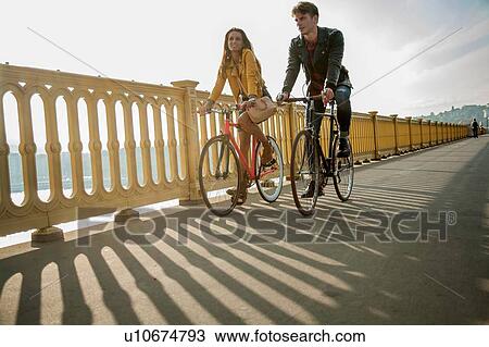 Stock Image - Couple crossing bridge on bicycles, Budapest, Hungary. Fotosearch