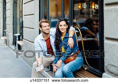 Stock Image - Couple sitting by shop window, Milan, Italy. Fotosearch
