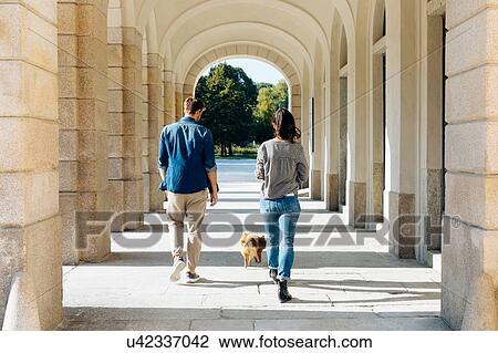 Stock Image - Couple with pet dog under arches of porticos, Milan, Italy. Fotosearch