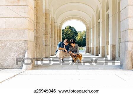 Stock Photograph - Couple with pet dog under arches of porticos, Milan, Italy. Fotosearch